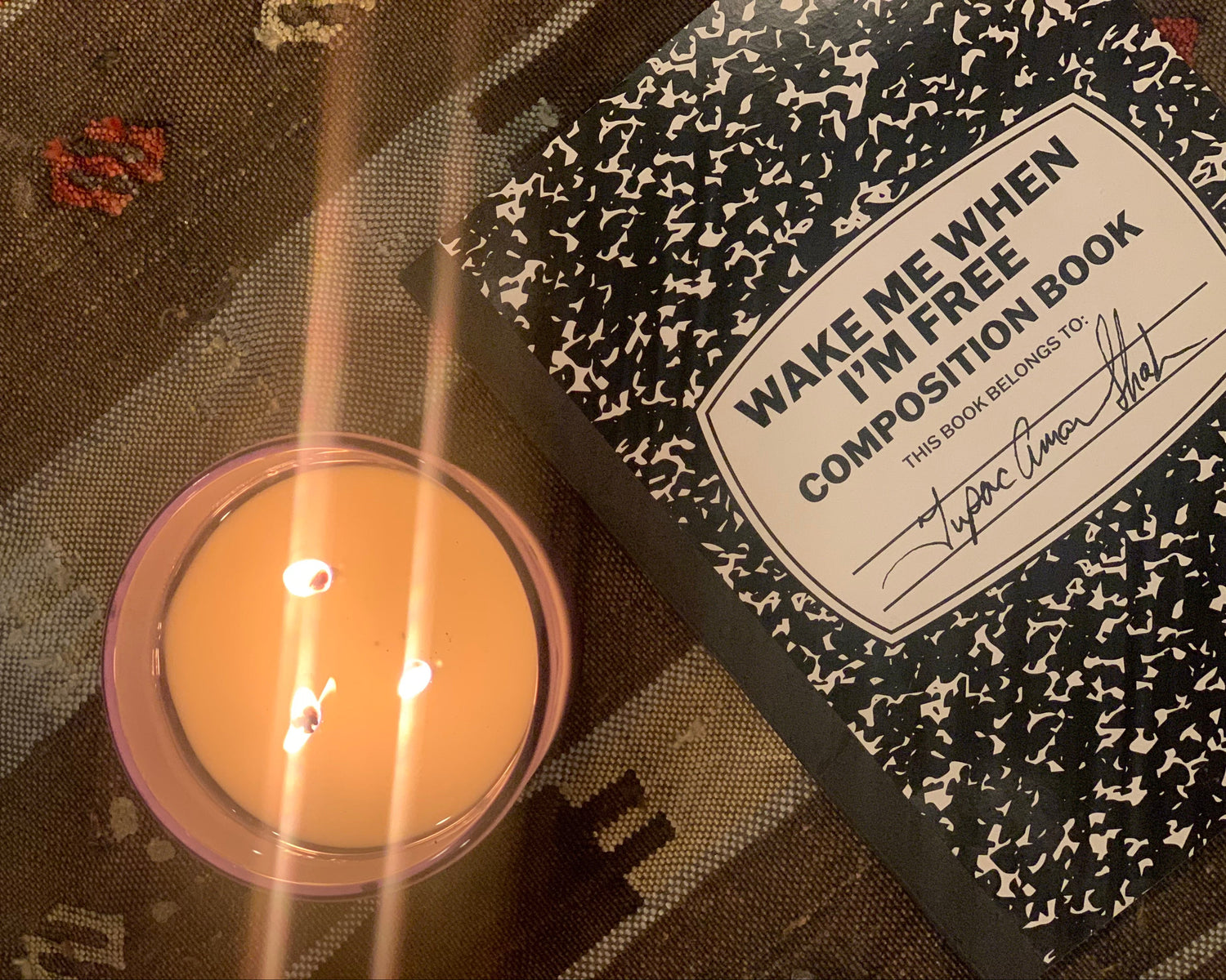 Candle next to a composition book titled 'Wake Me When I'm Free' on a textured surface.